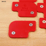 Red magnetic shims for woodworking, labeled with measurements, on a wood surface.