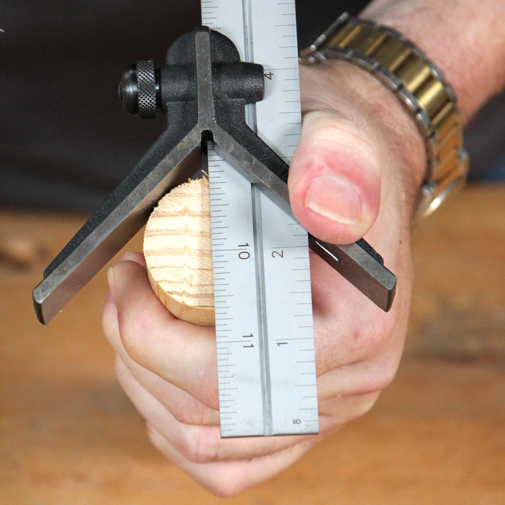 Woodworker using center finding tool and metal ruler on round wooden dowel