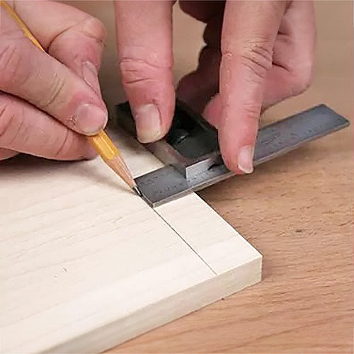 Woodworker marking a straight line on a board with a combination square and pencil
