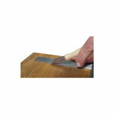 Hand using wood chisel and steel ruler on hardwood surface for precise woodworking