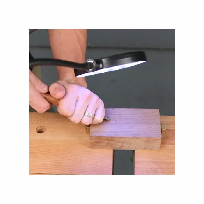 Woodworker using chisel on wood block with LED magnifying lamp for precision work