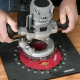 Woodworking router in use on a Milescraft base over a red saw blade jig on a workbench.