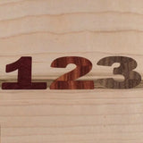 Wooden numbers 1, 2, and 3 cut from different hardwoods on a light wood background
