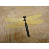 Wood inlay of a dragonfly design on a light wood surface, ideal for woodworking projects.