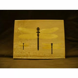Woodworking inlay panel with three dragonfly silhouettes on light wood background