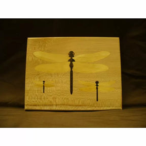 Woodworking inlay panel with three dragonfly silhouettes on light wood background