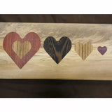 Wood inlay with four heart shapes in different colored woods on a light wood background
