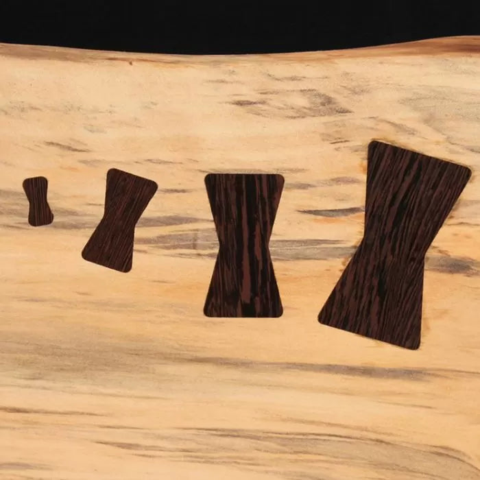 Close-up of four wooden bow tie inlays in light wood slab for woodworking joinery repair.