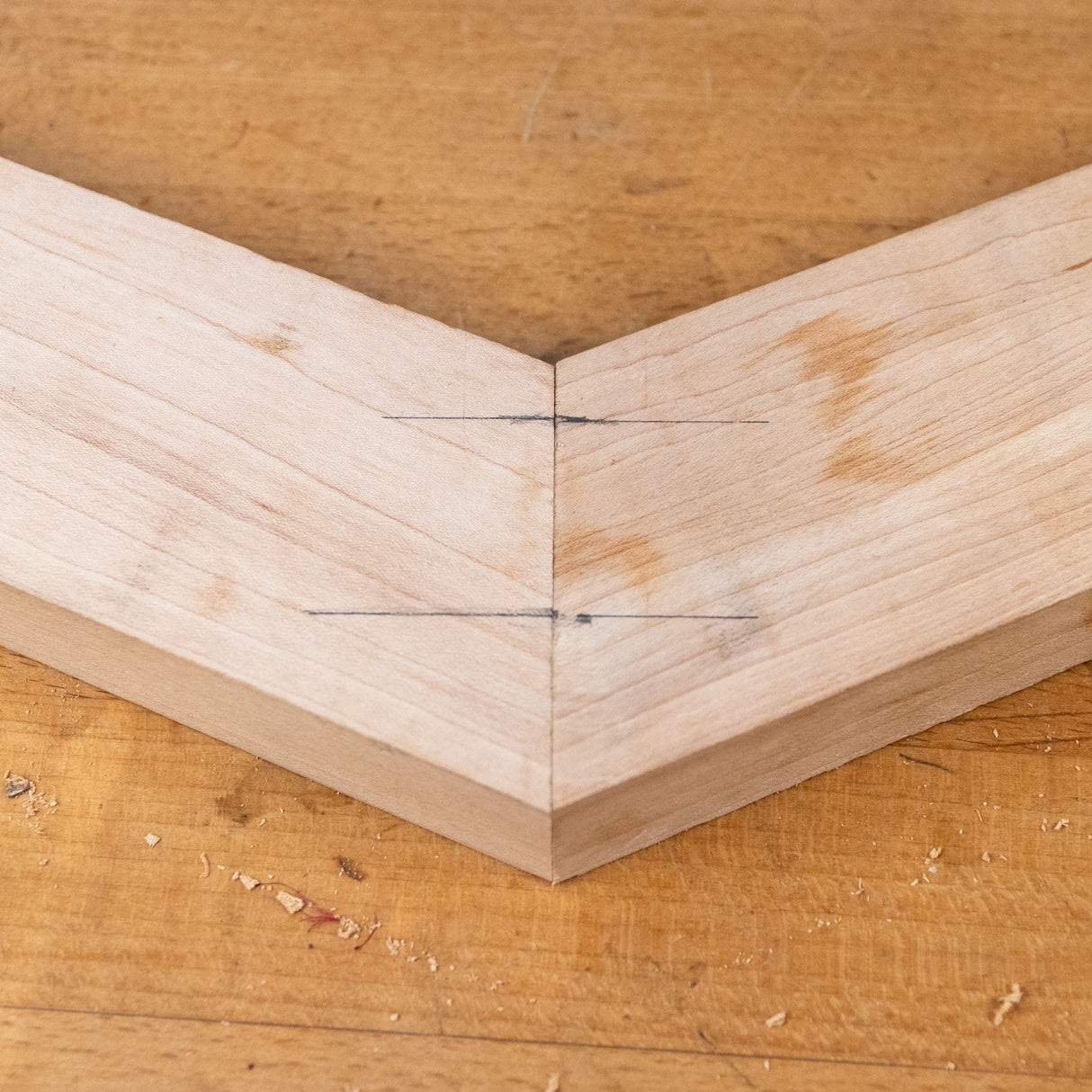 Close-up of a miter joint with dowel alignment marks on light wood, resting on a workbench