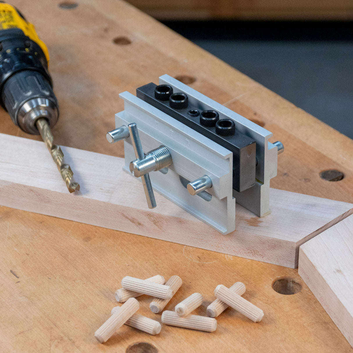 Self-centering dowel jig set on wood with drill and dowel pins on a workbench