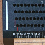 Close-up of woodworking jig with offset hole guide and inch measurements for precise drilling.
