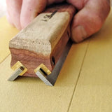 Woodworking marking gauge tool with dual blades and wooden handle in use on yellow work surface