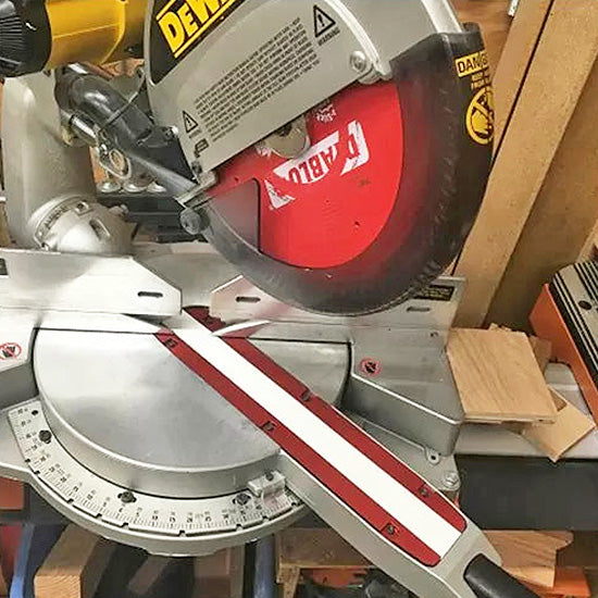 Miter saw with red carbide blade and table gauge in woodworking shop