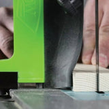 Close-up of a bandsaw cutting a piece of wood with a safety guide and operator's hand