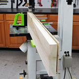 Band saw with resaw guide and push block cutting hardwood board in woodworking shop