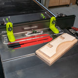 Table saw with L-fence system, safety featherboards, and wooden workpiece in workshop