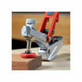 Toggle clamp with red handle securing wood on workbench, woodworking tool close-up