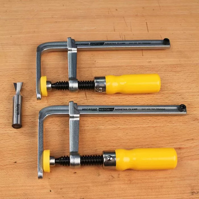 Dovetail clamps with yellow handles and a dovetail router bit on a wood workbench