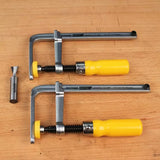 Dovetail clamps with yellow handles and a dovetail router bit on a wood workbench