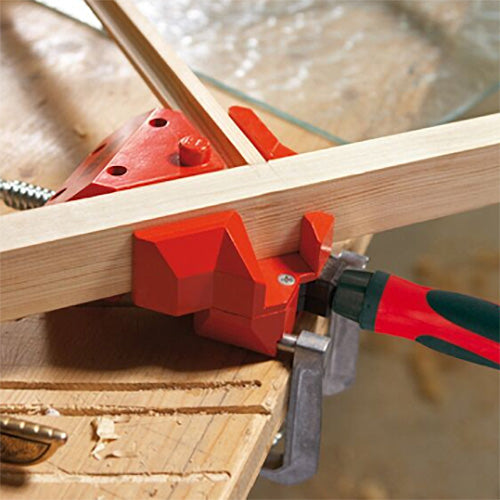 Woodworking corner clamp securing two boards at a right angle on a workbench