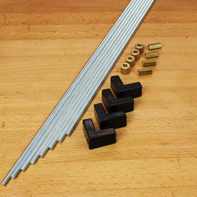 Woodworking jig hardware kit with threaded rods, black plastic brackets, and brass fittings on a workbench.
