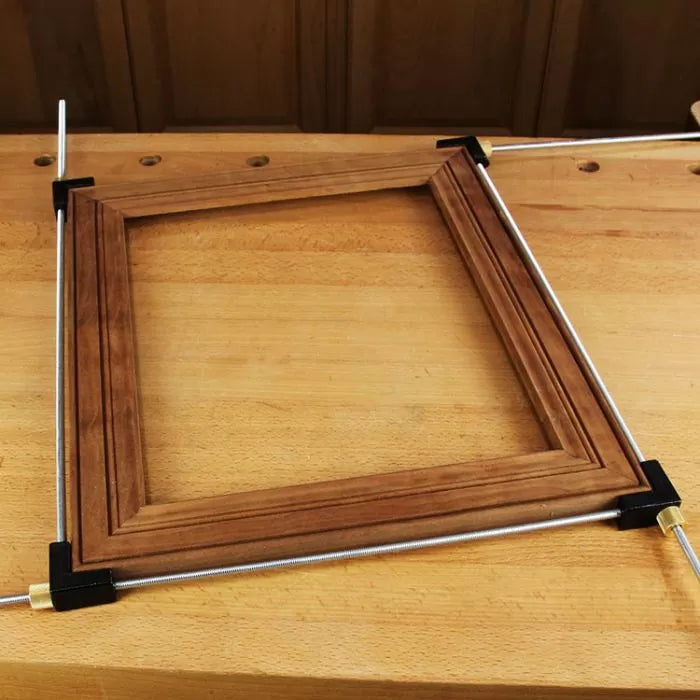 Woodworking picture frame held by corner clamps and steel rods on a workbench