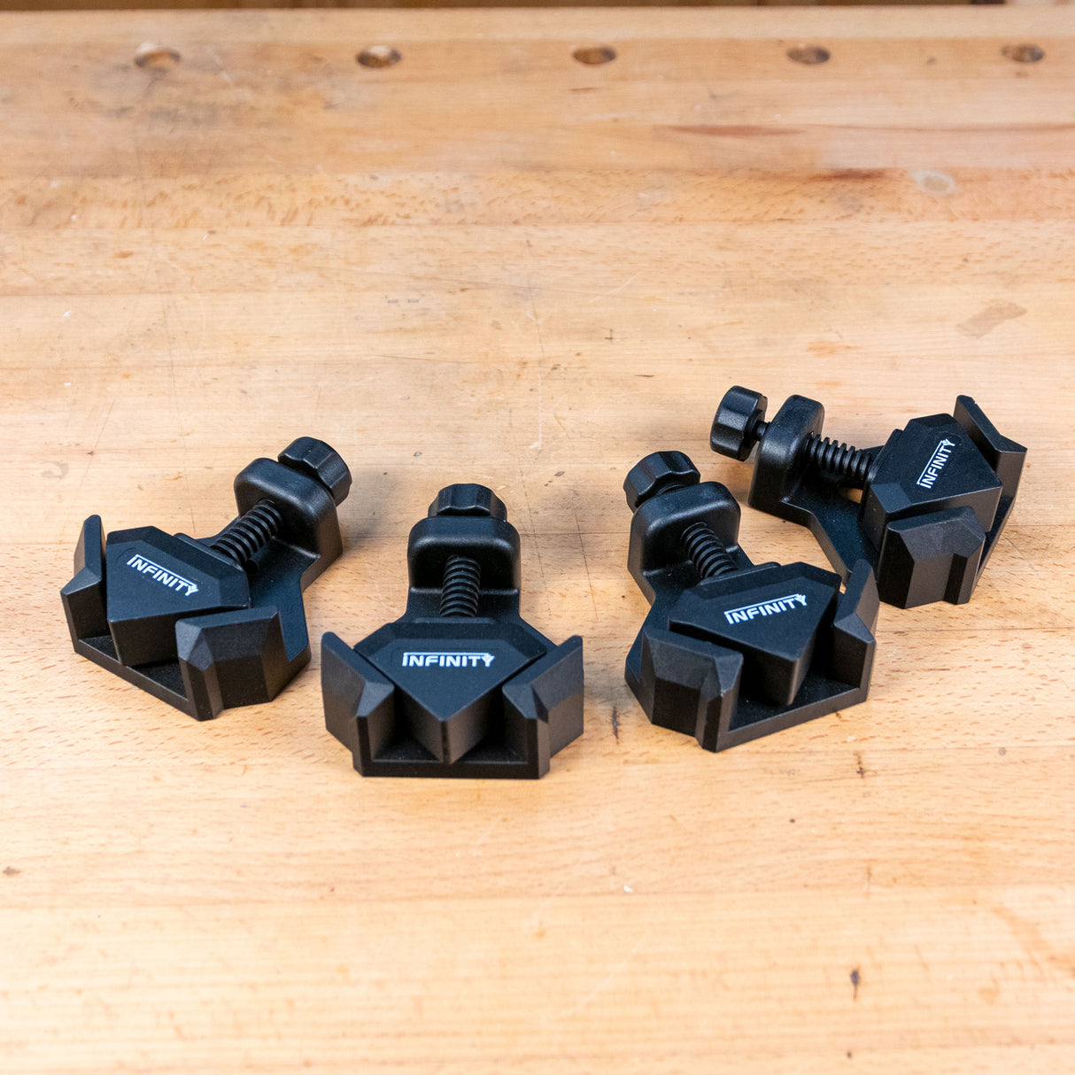 Set of four black corner clamps for woodworking on a wooden workbench surface