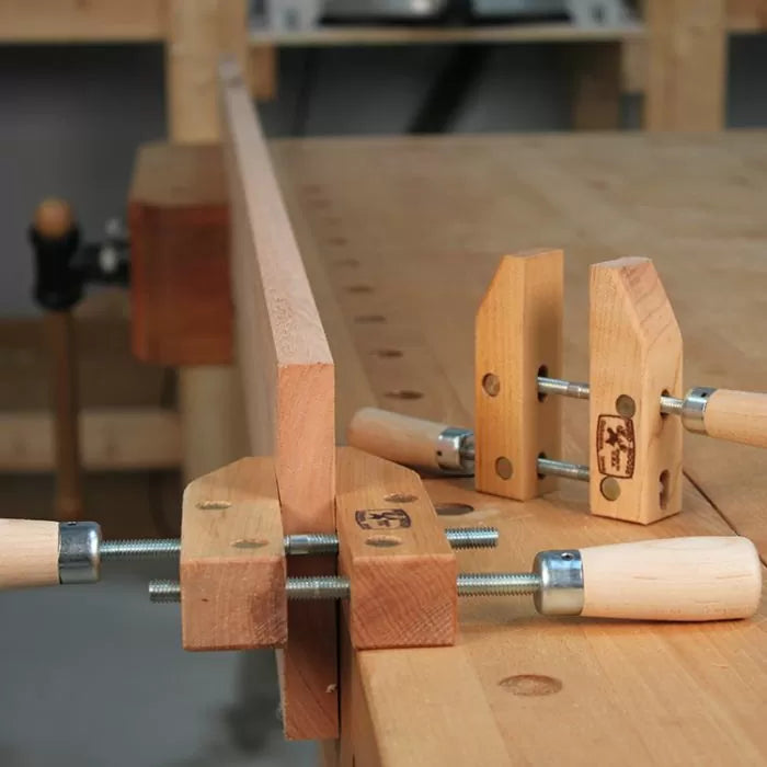 Wooden handscrew clamps securing a board on a workbench in a woodworking shop