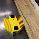 Yellow woodworking featherboard attached to table saw holding wooden board securely.