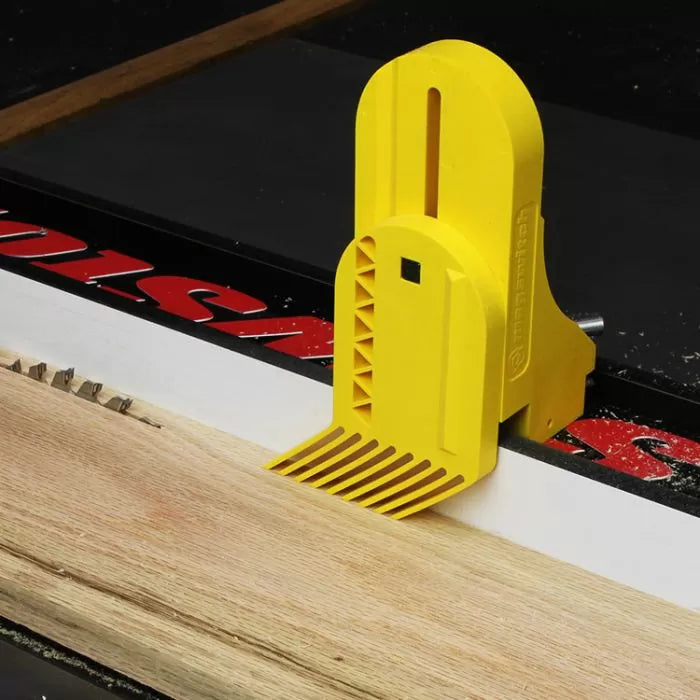 Yellow table saw featherboard holding wood against fence for precise woodworking cuts