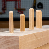 Four wooden dowels on a wooden block with a blurred workshop background