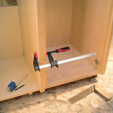 Bar clamp securing wood panel in cabinet assembly on woodworking bench