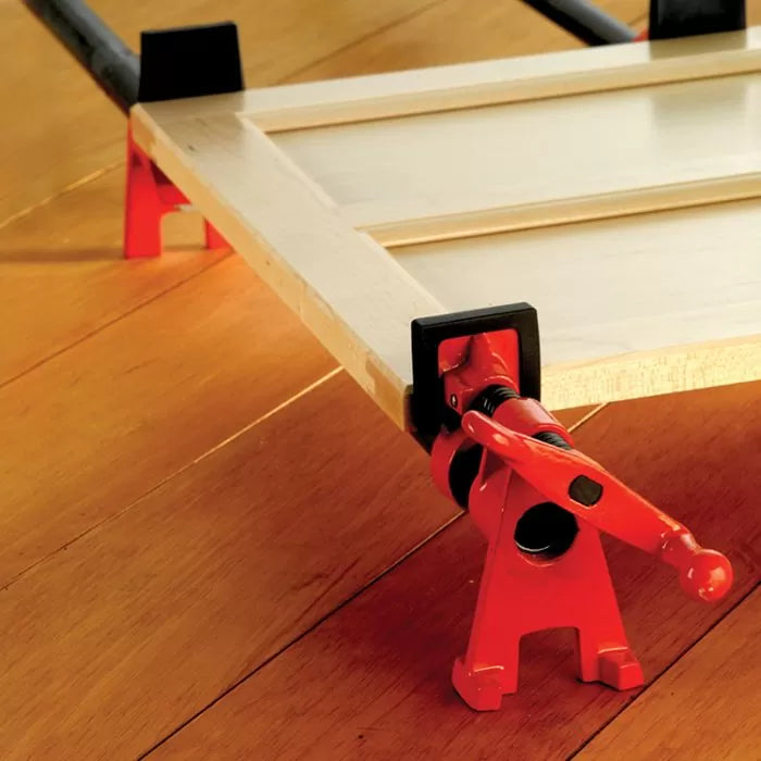 Woodworking pipe clamp holding a cabinet door panel on a hardwood floor