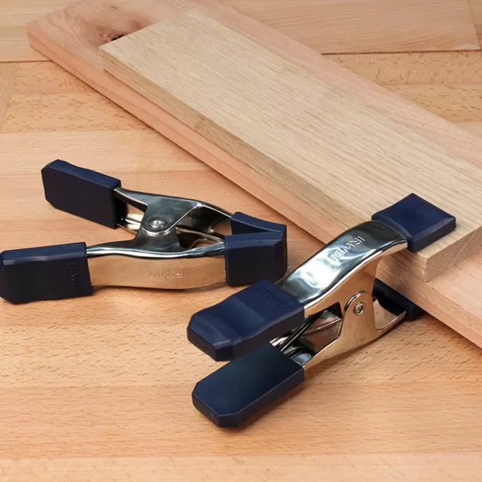 Metal spring clamps with blue rubber grips holding wood on a workbench, woodworking tools
