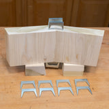 Metal pinch dogs for woodworking displayed with joined wood blocks on a workbench