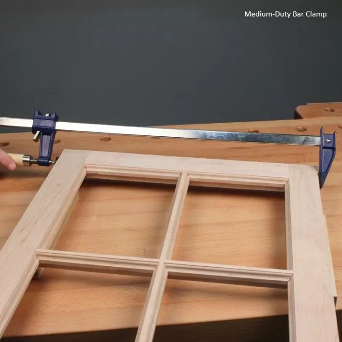 Medium-duty bar clamp securing wooden window frame on workbench for woodworking projects