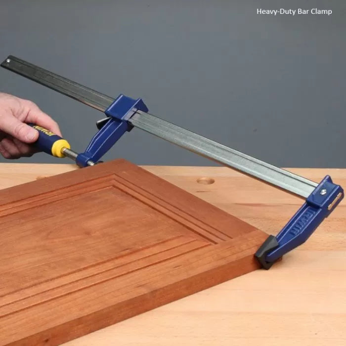 Heavy-duty bar clamp securing a wooden cabinet door on a workbench, woodworking tool