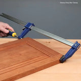 Heavy-duty bar clamp securing a wooden cabinet door on a workbench, woodworking tool