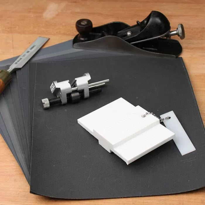 Woodworking hand tools, sharpening jig, and sanding sheets on a workbench surface