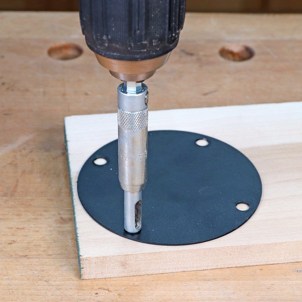 Drill with self-centering bit making a pilot hole in a router table insert plate on wood