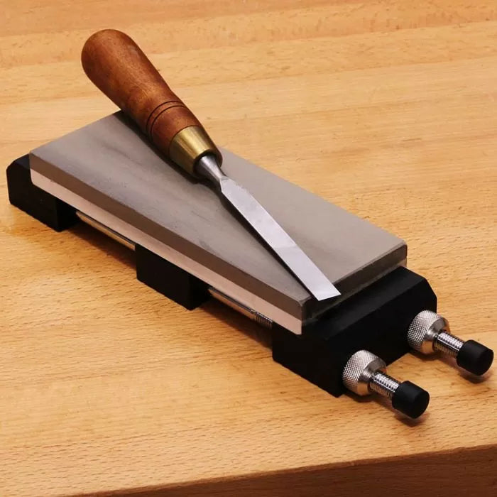 Sharpening stone with wood handle chisel on adjustable honing guide, placed on workbench