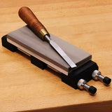 Sharpening stone with wood handle chisel on adjustable honing guide, placed on workbench
