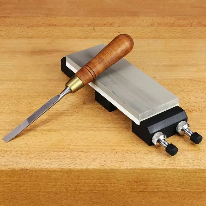 Woodworking chisel with wood handle resting on sharpening stone with holder on workbench
