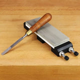 Woodworking chisel with wood handle resting on sharpening stone with holder on workbench