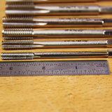 Thread cutting taps lined up next to a metal ruler on a woodworking table