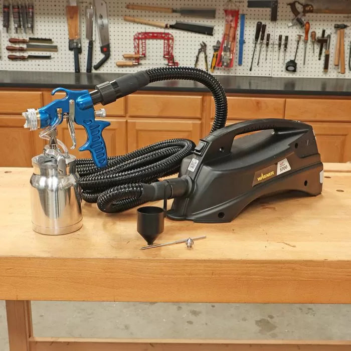 Wagner paint sprayer system with blue spray gun and hose on a woodworking bench