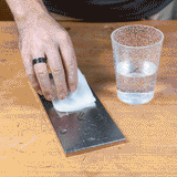 Hand wiping sharpening stone with damp cloth on woodworking bench, water glass nearby