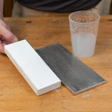 Sharpening stone and flattening plate on workbench with water cup, woodworking tools