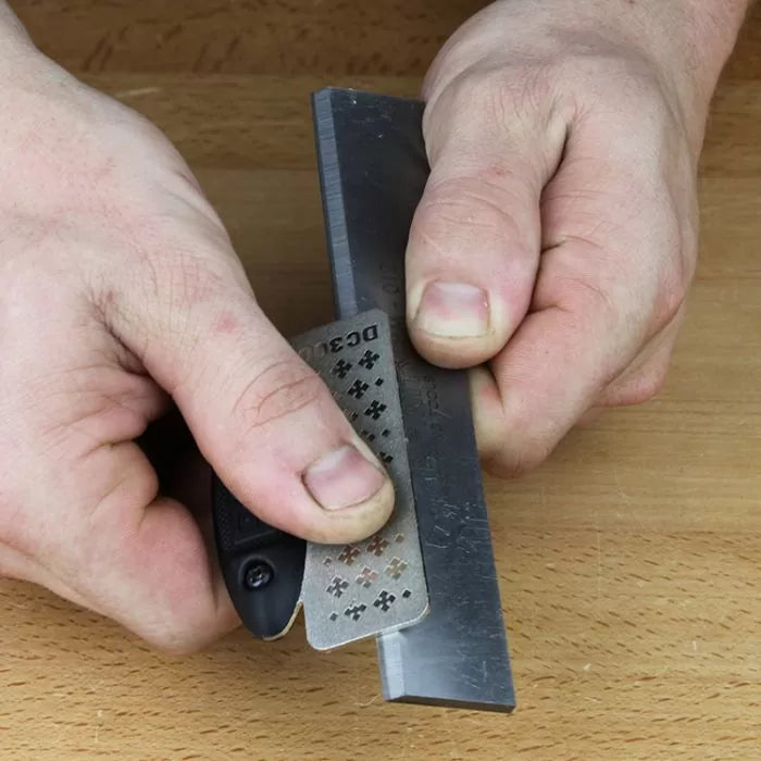 Sharpening a woodworking chisel with a diamond sharpening card on a wooden workbench