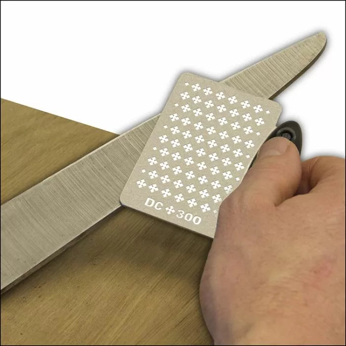 Hand sharpening a knife blade with a DC300 diamond sharpening card on wood surface